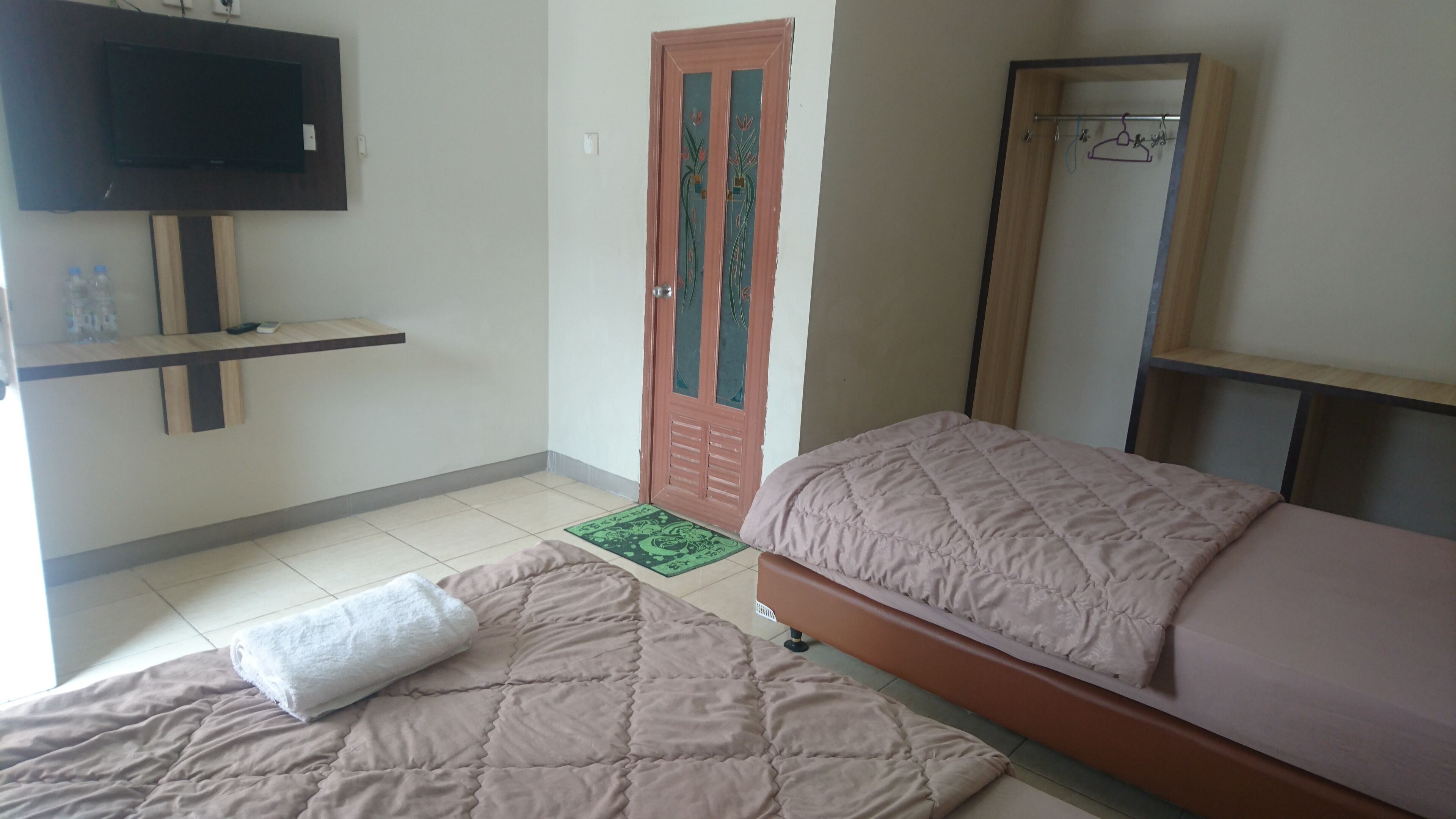 A bedroom with two beds, a TV mounted on the wall, a wardrobe, and a door with decorative glass panels.