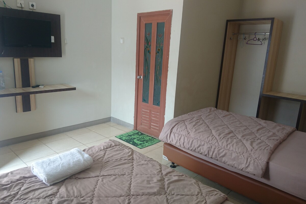 A hotel room with a bed, a TV mounted on the wall, a wooden shelf, and a door with decorative glass panels.