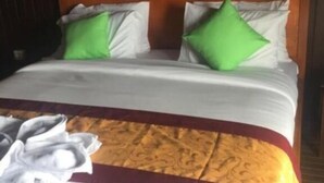Een hotelkamer met een houten hoofdeinde, witte beddengoed en groene kussens.