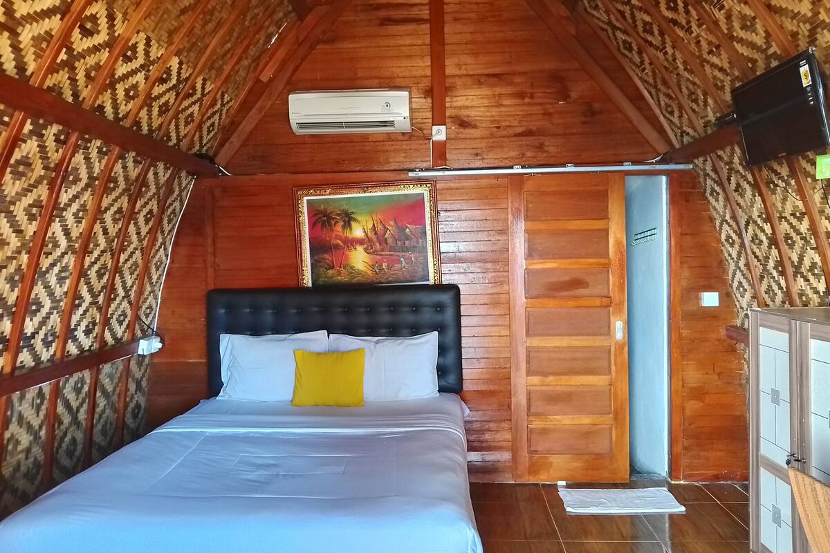 A bedroom with a bed, a painting, an air conditioning unit, and a wooden ceiling.