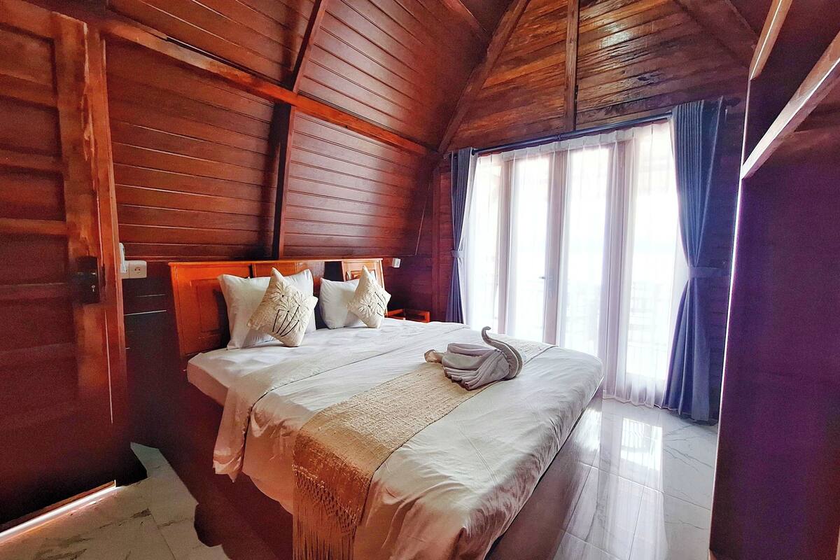 A wooden-paneled room with a bed, pillows, and a towel.