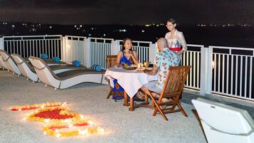 A dining area with a table set for two, surrounded by lounge chairs, and a decorative arrangement of candles and flowers on the floor.