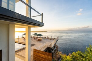 A modern outdoor terrace with a view of the sea, featuring outdoor seating and a wooden deck.
