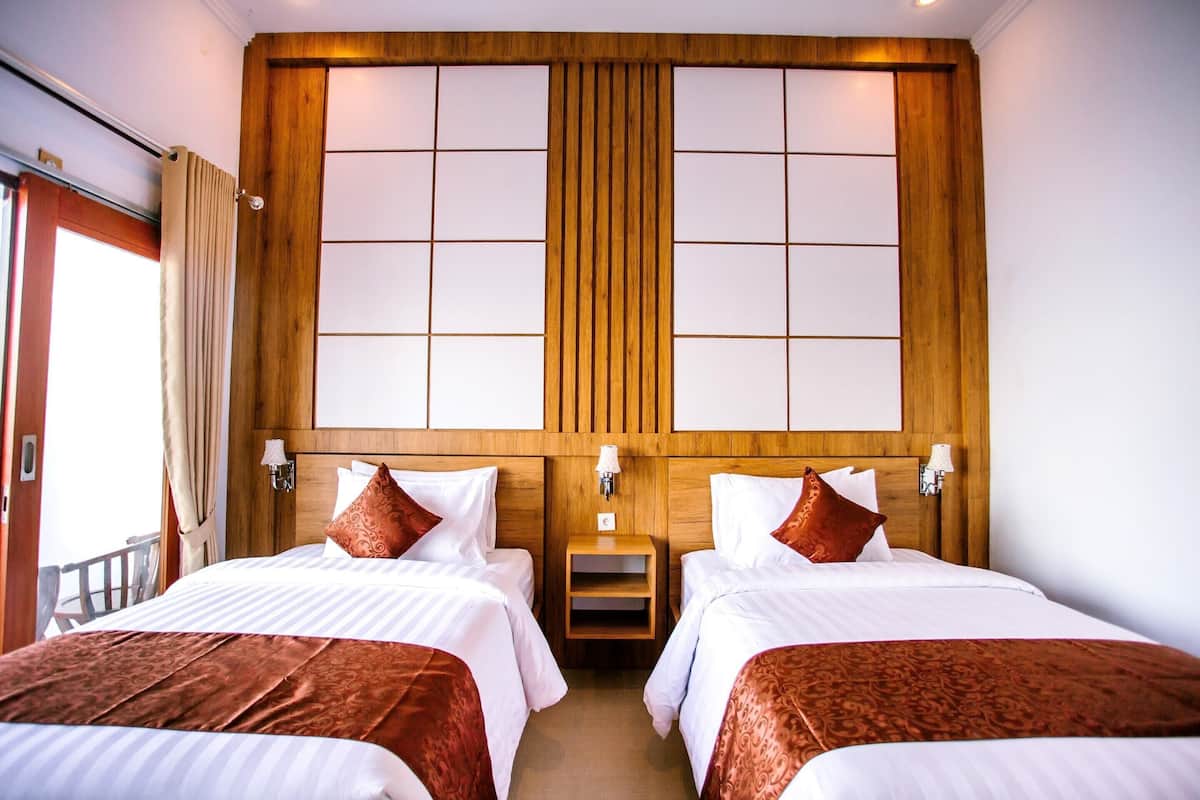 Habitación de hotel con dos camas, cabecera de madera, lámparas de noche y mesitas de noche.