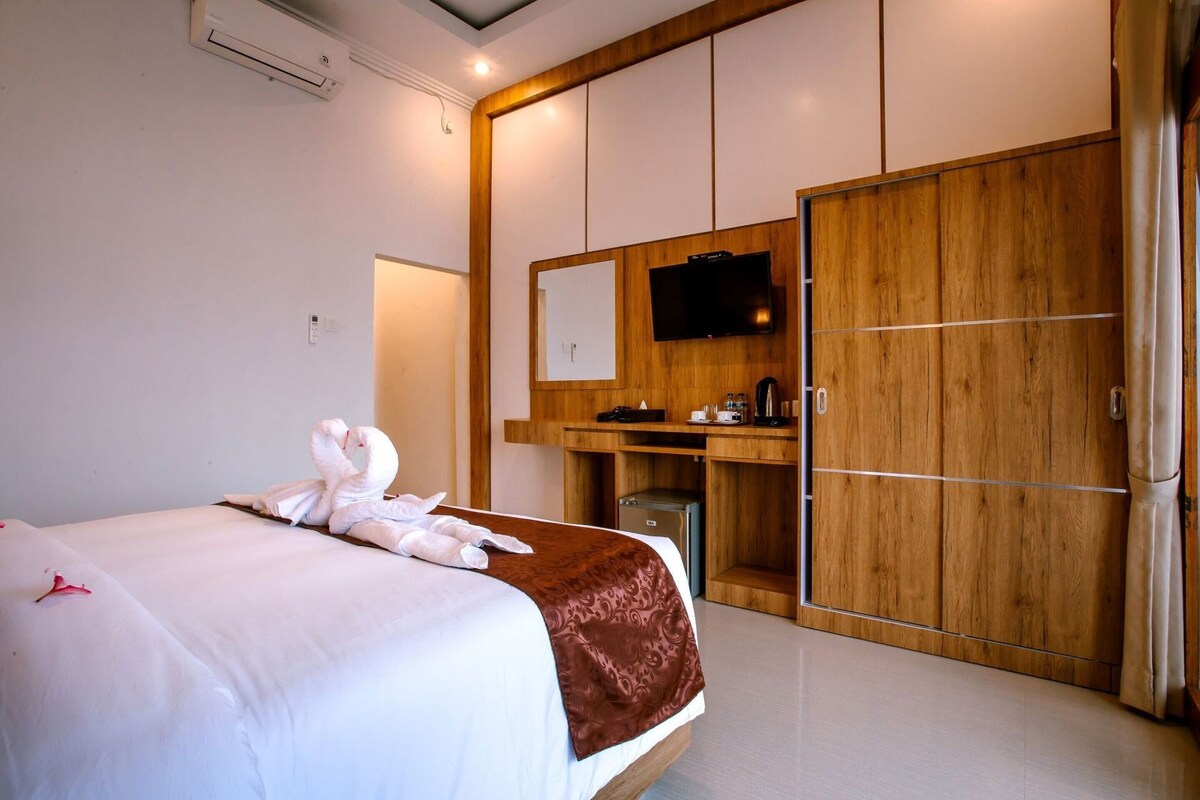 A hotel room with a bed, a wooden wardrobe, a desk with a flat-screen TV, and a minibar.