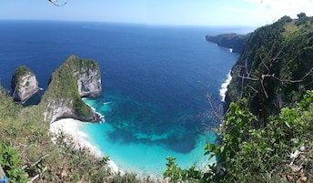 Paisaje costero con acantilados, aguas turquesas cristalinas y una playa.