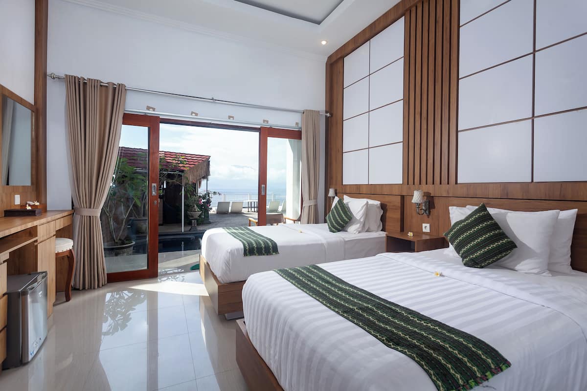 Habitación de hotel con dos camas, cabecera de madera, escritorio y vista al mar.