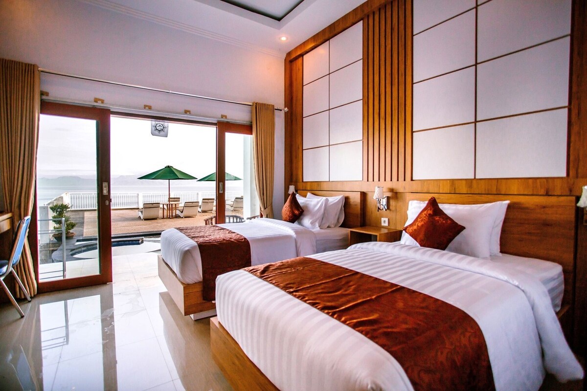 A hotel room with two beds, a large window, and a view of the beach.