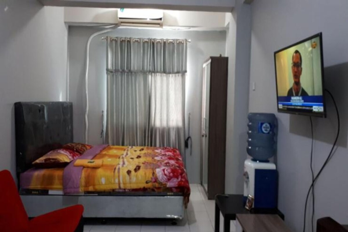 A hotel room with a bed, a television, a water dispenser, and a red chair.
