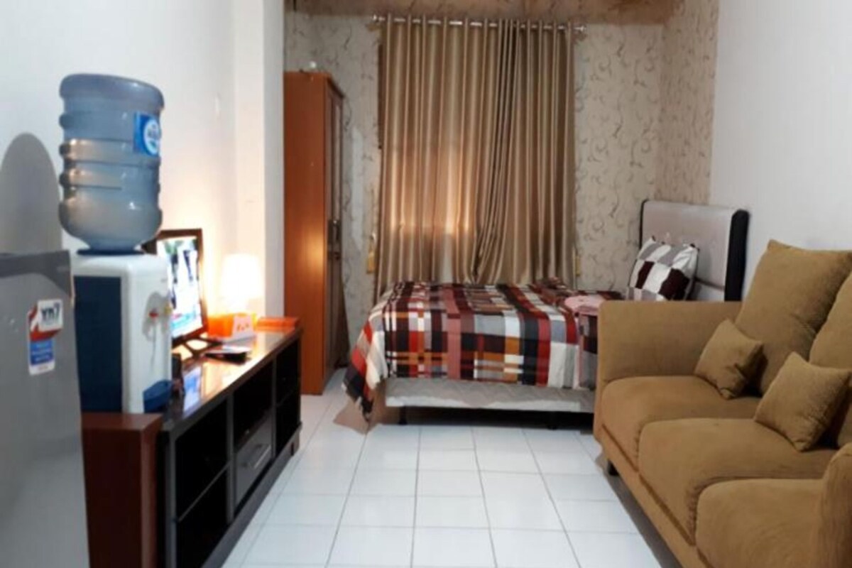 A hotel room with a bed, a sofa, a desk with a computer, and a water dispenser.