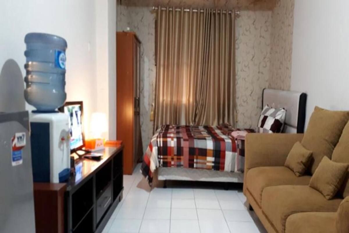 Een kleine hotelkamer met een bed, een slaapbank, een bureau met een computer en een waterdispenser.