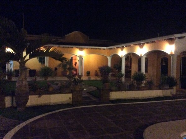 A courtyard with a pool, potted plants, and a building with multiple arches and lights.