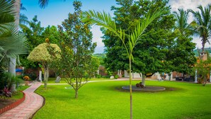 Jardim bem cuidado com um caminho de tijolos, área de gramado circular e diversas árvores.