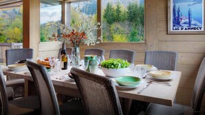 Een eethoek met een tafel voor vier personen, omringd door rieten stoelen, met uitzicht op een bos door grote ramen.