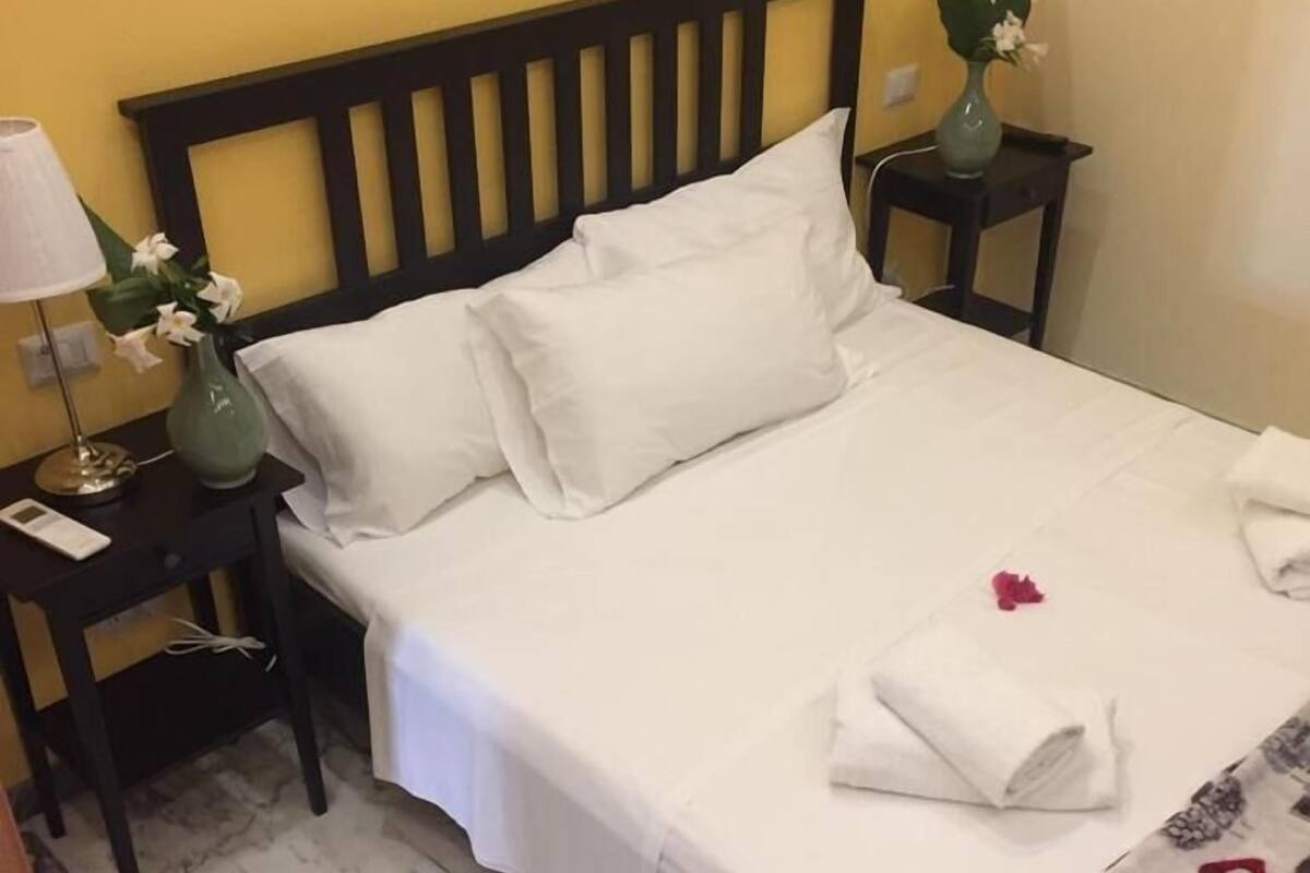 A hotel room with a bed, two nightstands, a vase with flowers, and a marble floor.