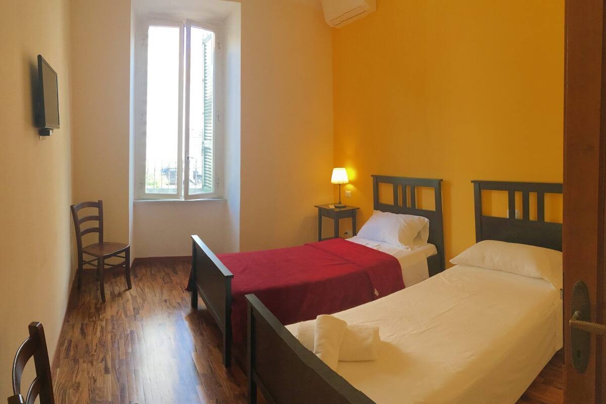 A room with two beds, a chair, a TV, and a window with blinds.