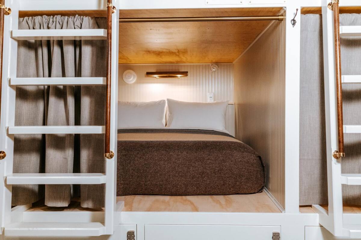 A compact, well-lit sleeping area with a bed, curtains, and a small shelf.