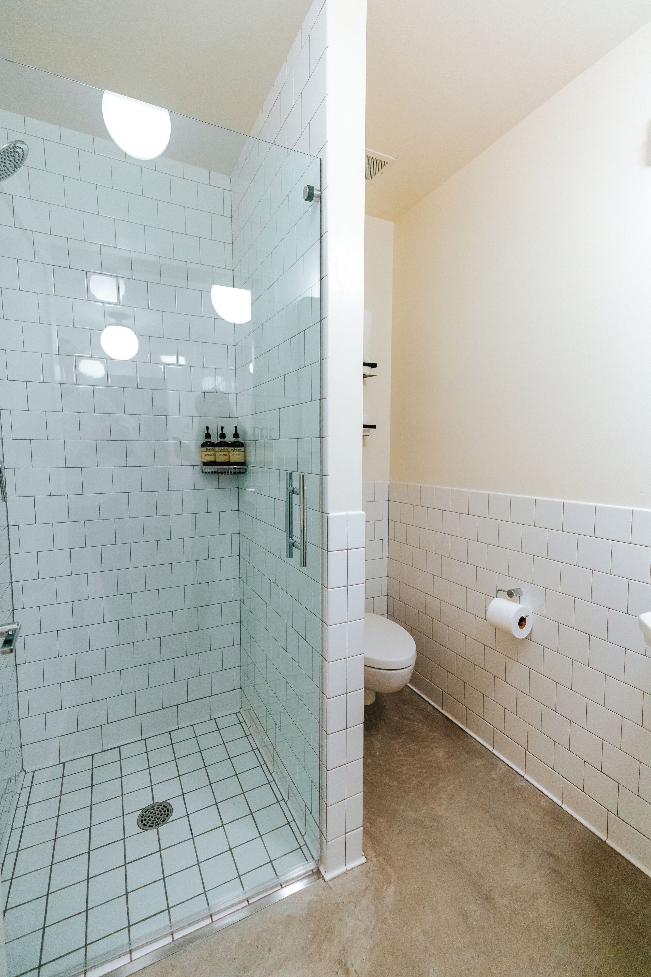 A bathroom with white tiled walls, a glass shower enclosure, a toilet, and a sink.
