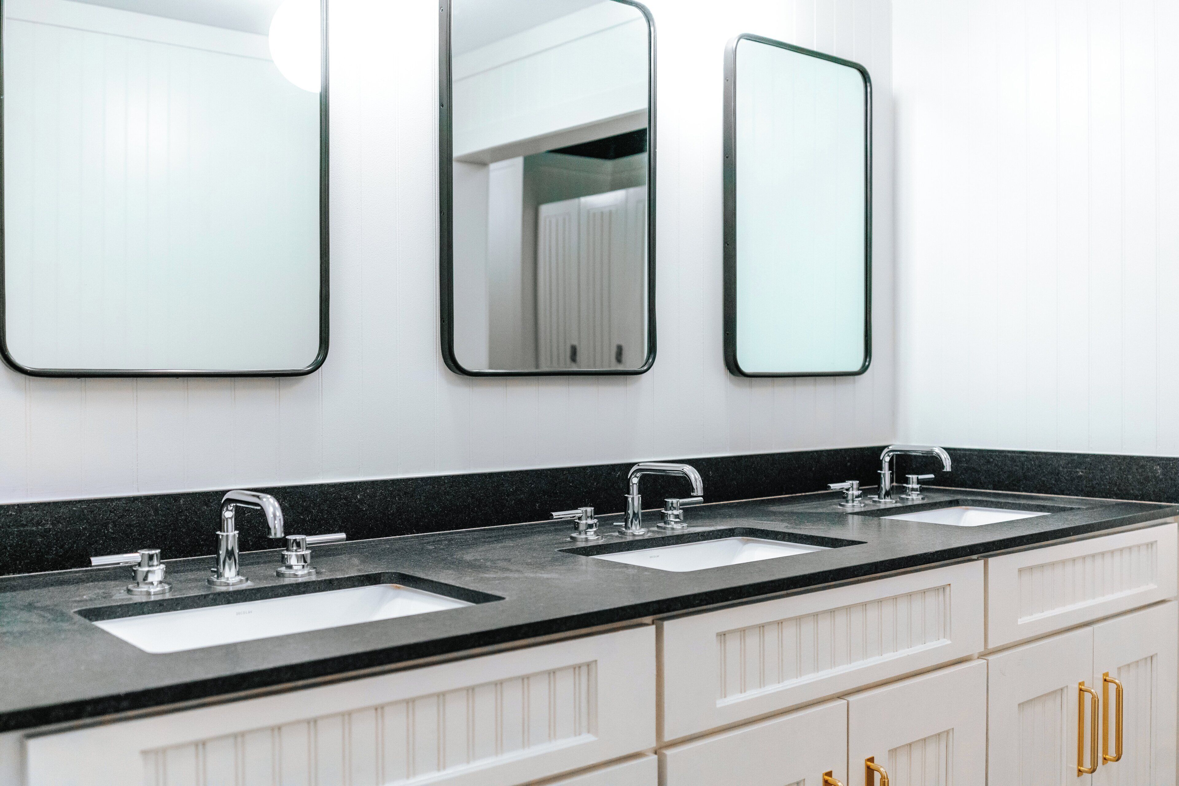 A bathroom with two sinks, three mirrors, and white cabinetry.