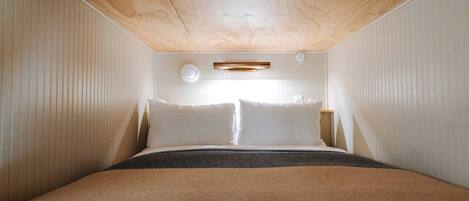 A bedroom with a wooden ceiling, a bed with white bedding, and a small bedside table.