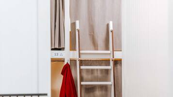 Ein Zimmer mit einem Etagenbett, einer Leiter, einer roten Jacke, die an der Wand hängt, und einem gestreiften Teppich auf dem Boden.
