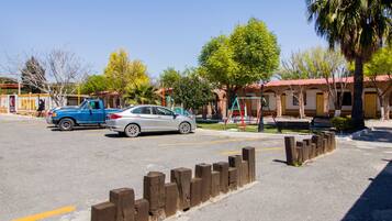A hotel with a red-tiled roof, a playground, and a parking lot with a blue truck and a silver car.