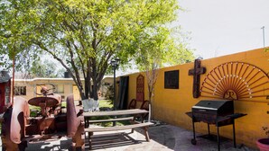 An outdoor patio with a wooden table, a bench, a grill, and a vintage tractor. - Hotel Santa Rosa (General Cepeda)