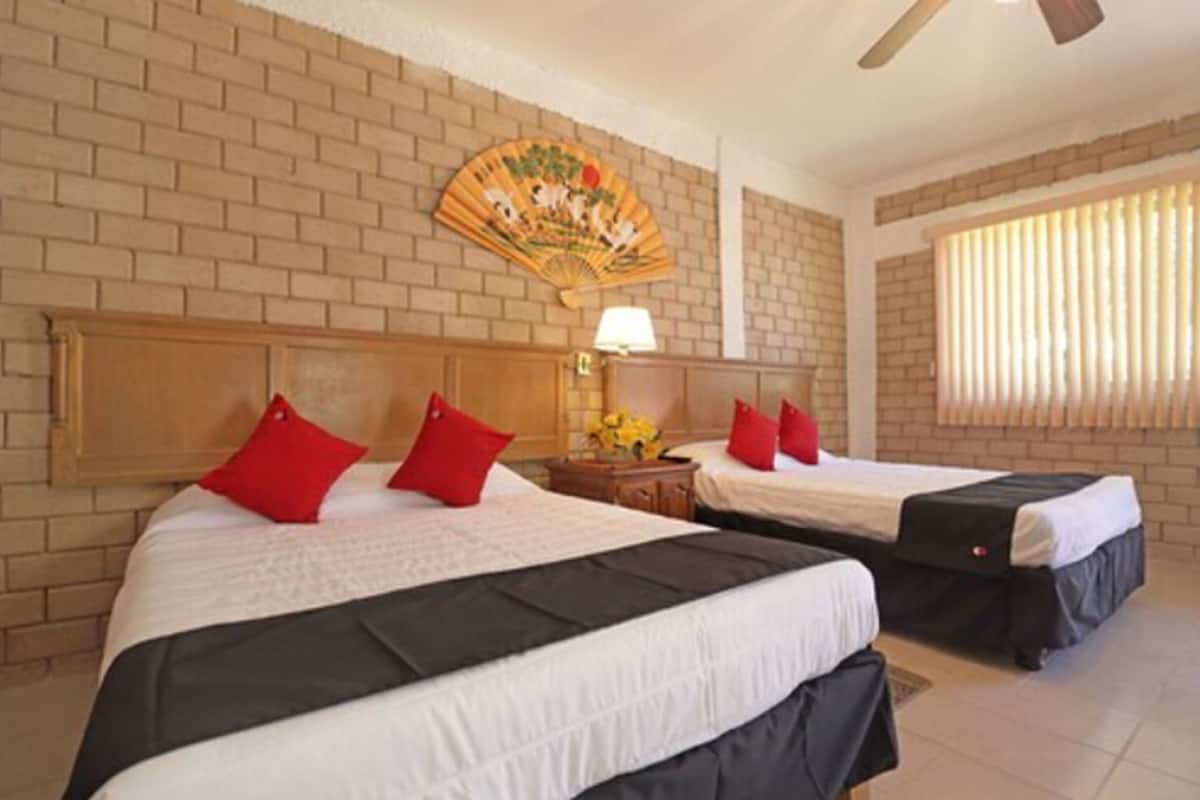 A hotel room with two beds, a brick wall, a ceiling fan, and a window with blinds.