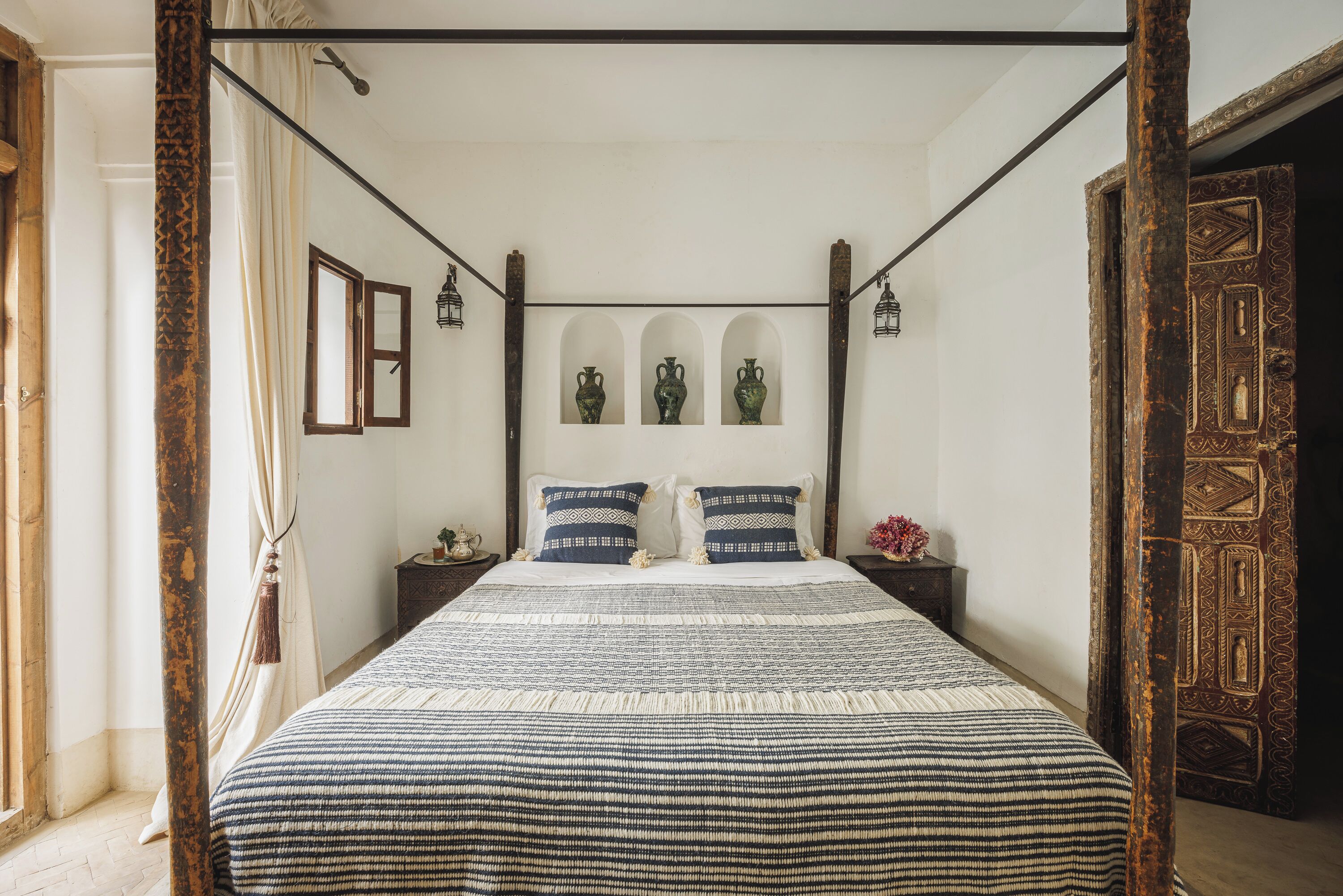 A four-poster bed with a patterned bedspread and matching pillows, flanked by nightstands with decorative items.