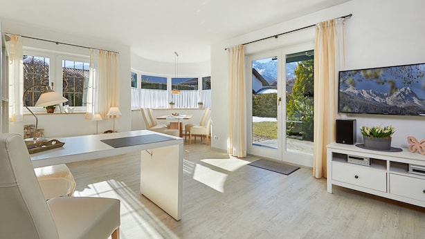 Un salon moderne et bien éclairé, doté d’un grand téléviseur, d’un coin repas et d’une porte-fenêtre coulissante donnant sur un balcon avec vue sur les montagnes.