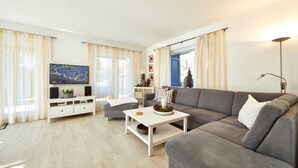 Un salon moderne avec un canapé gris, une table basse blanche et un téléviseur à écran plat posé sur un meuble blanc.