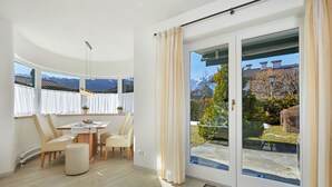 Une chambre moderne dotée d’un coin repas, d’une grande porte-fenêtre coulissante donnant sur un jardin et offrant une vue sur les montagnes.