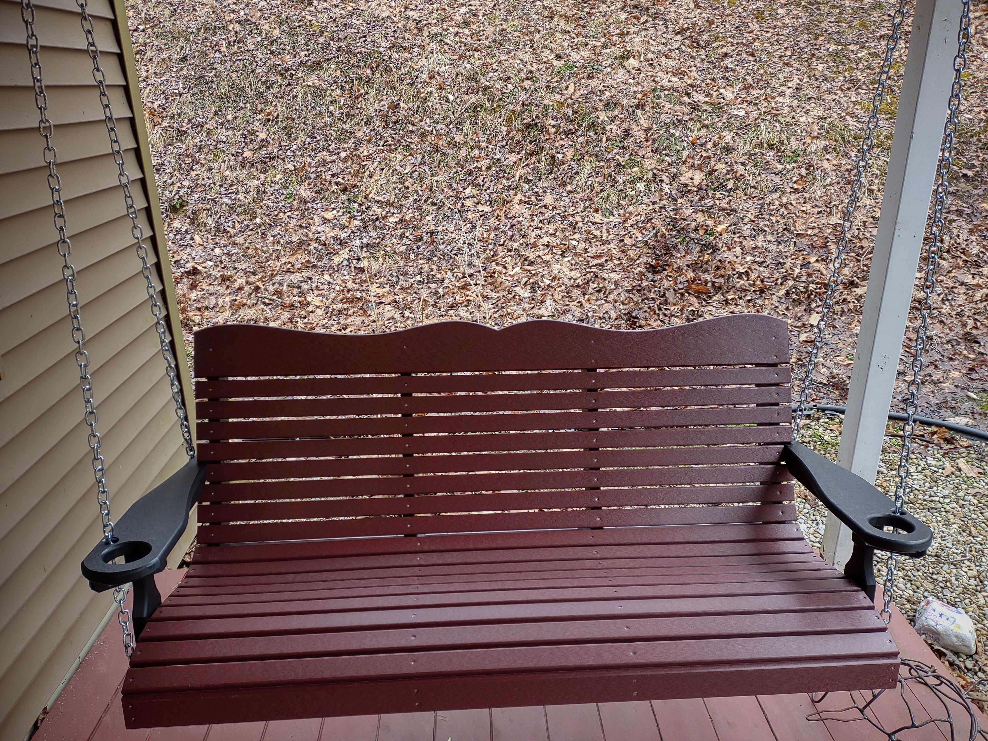 Een houten bank met metalen kettingen op een veranda.