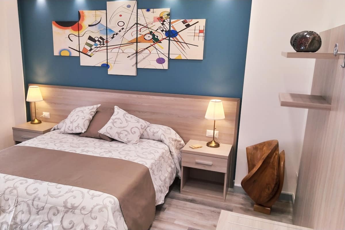 A hotel room with a large bed, two bedside tables with lamps, a wooden headboard, and abstract wall art.