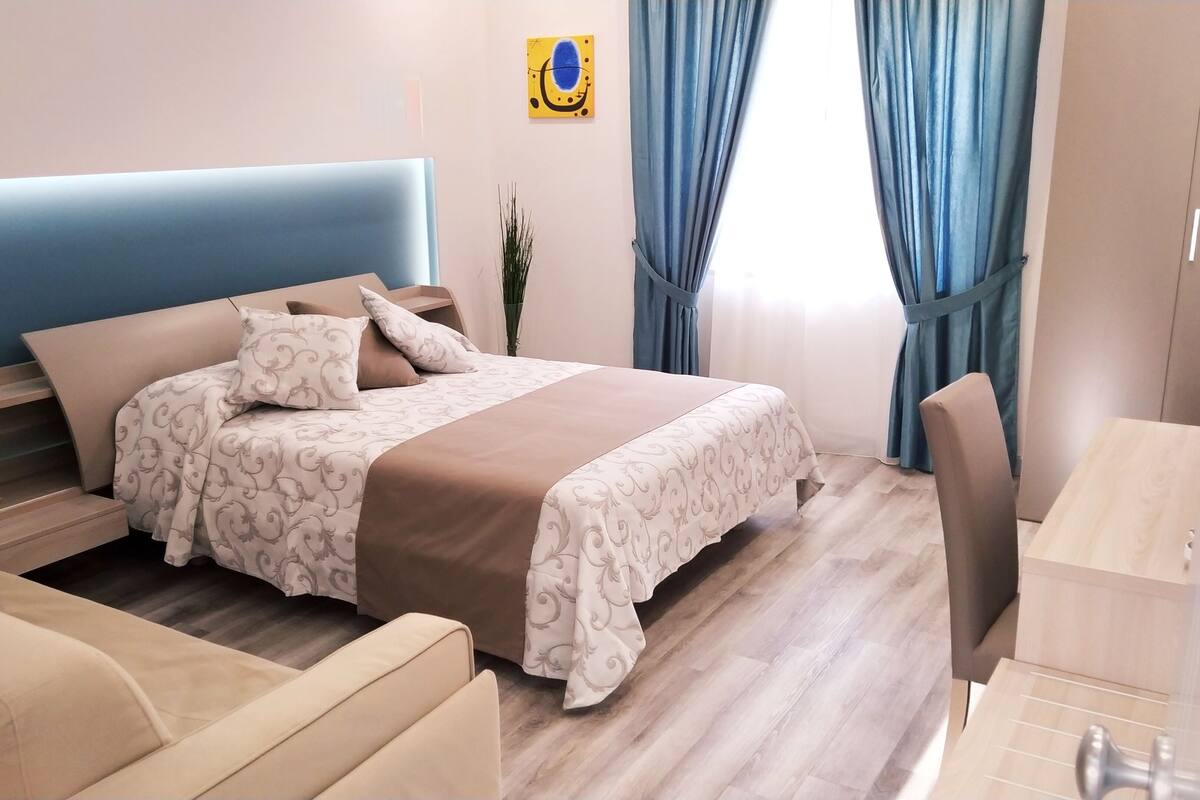 A neatly arranged hotel room with a bed, a desk, and a chair.