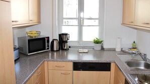 Cozinha com armários de madeira, micro-ondas, cafeteira, pia e janela com persianas.