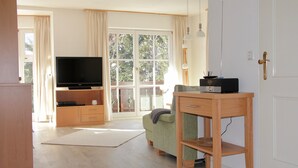 Uma sala de estar moderna com televisão de tela plana, uma mesa de madeira, um sofá e uma janela grande com cortinas.