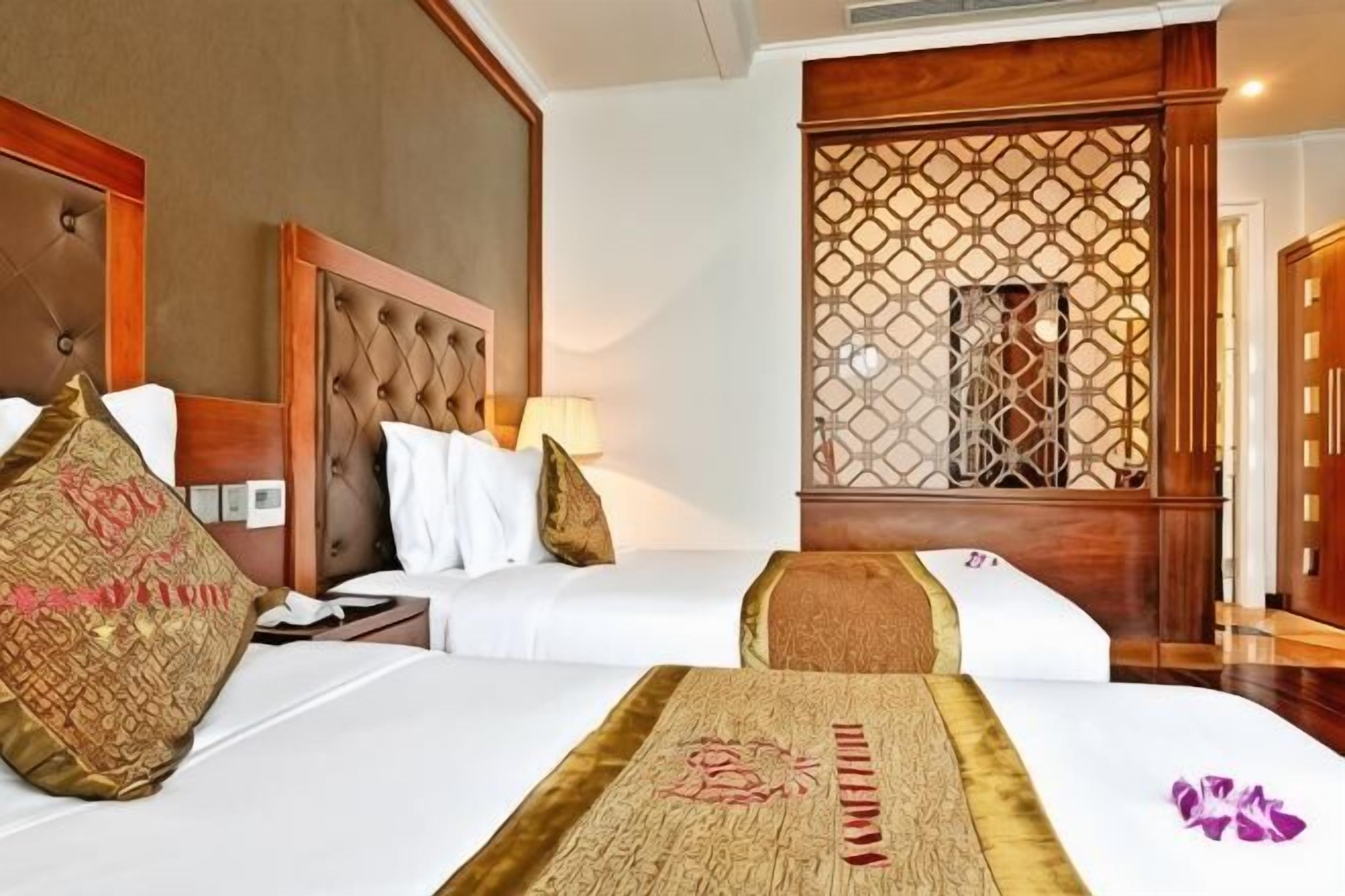 Une chambre d’hôtel avec deux lits, une tête de lit en bois, un paravent décoratif et une table de chevet avec une lampe.