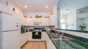 Cocina compacta con muebles blancos, microondas, horno, lavaplatos y encimera de granito.