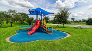 A playground with a slide and climbing structure, surrounded by grass and trees. - Royal_palm_bay_99 (Kissimmee)