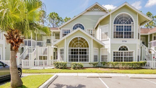 A large, two-story building with a symmetrical facade, large arched windows, and a white picket fence surrounding the property. - Royal_palm_bay_99 (Kissimmee)
