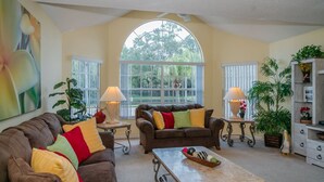 A living room with two brown leather sofas, a coffee table, and two lamps. There are large windows with white blinds, and a painting is visible on the wall. - Royal_palm_bay_99 (Kissimmee)