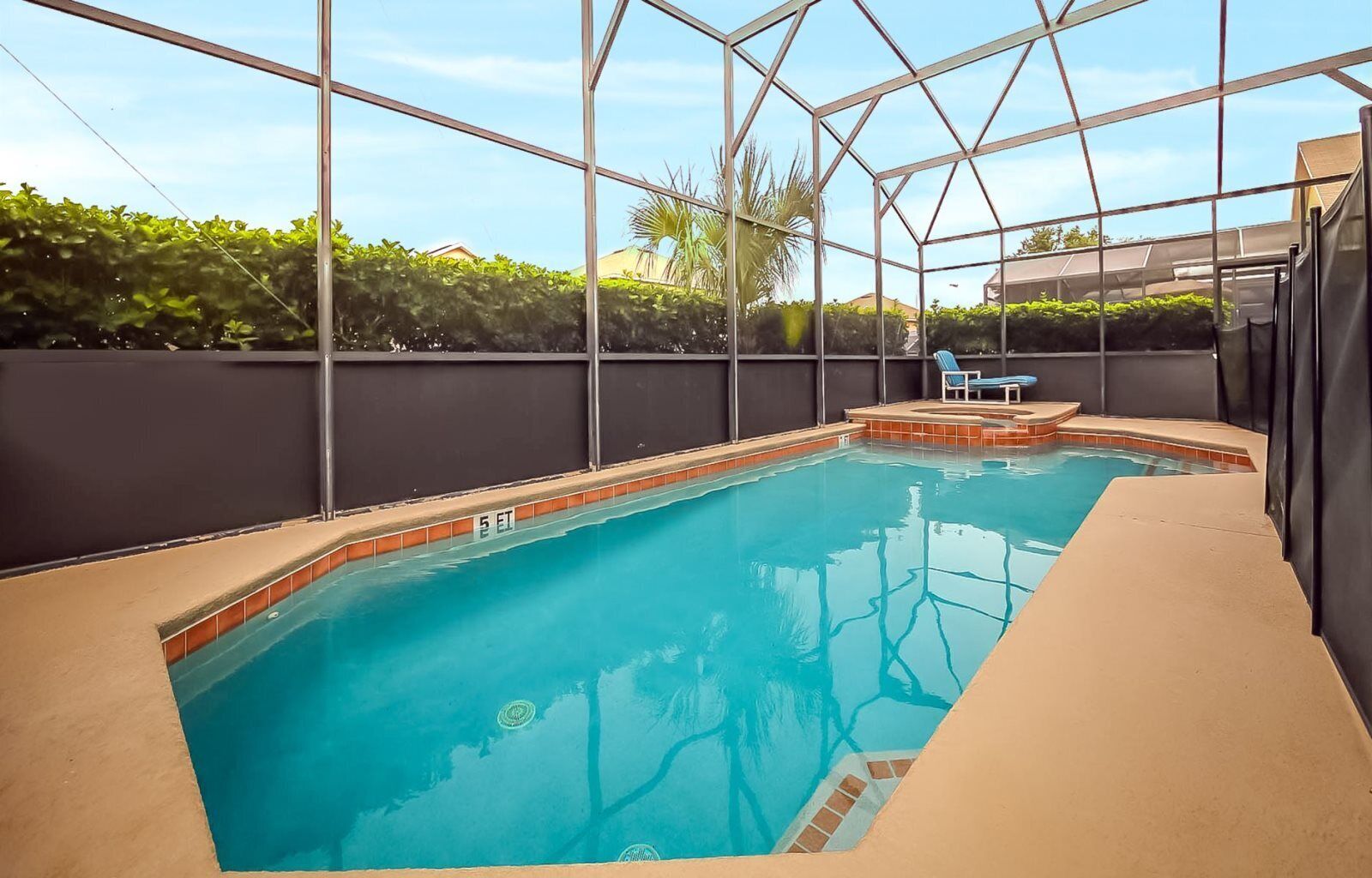 Una piscina con agua cristalina azul, rodeada por un recinto de vidrio, y una silla de descanso visible al fondo.