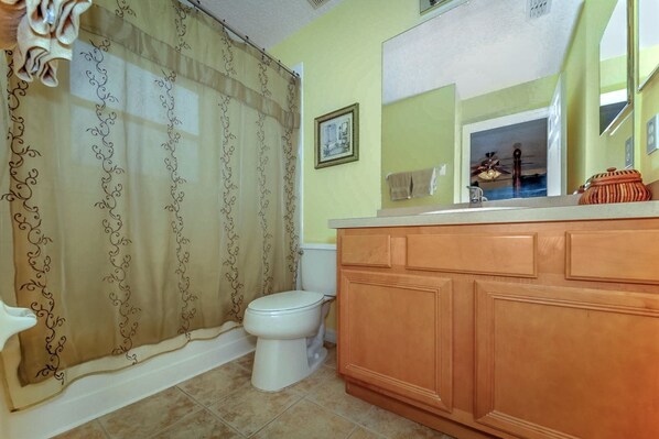 A bathroom with a toilet, a wooden vanity, a mirror, and a shower curtain.