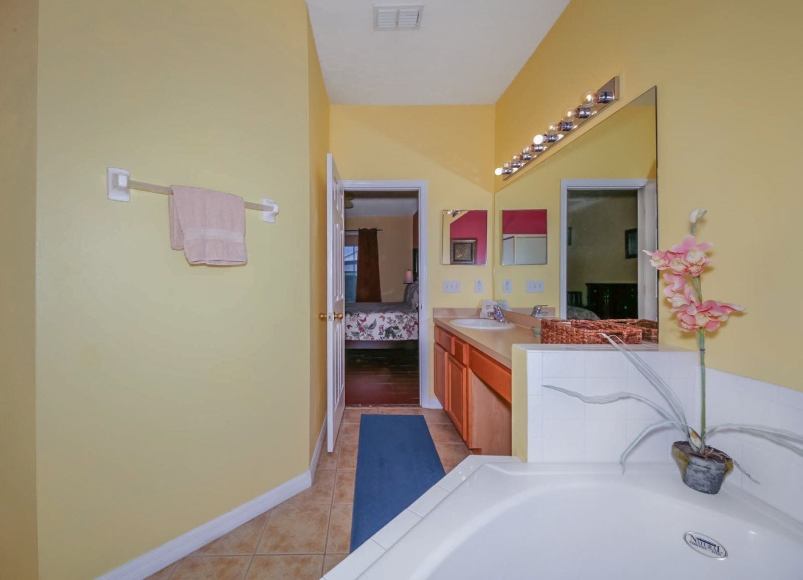 Un baño con una bañera, lavamanos, espejo y una orquídea en maceta.