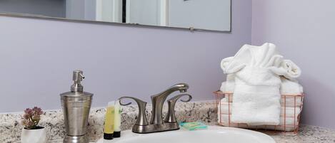 Un baño con lavamanos blanco, dos grifos, dispensador de jabón y toallero con toallas dobladas.