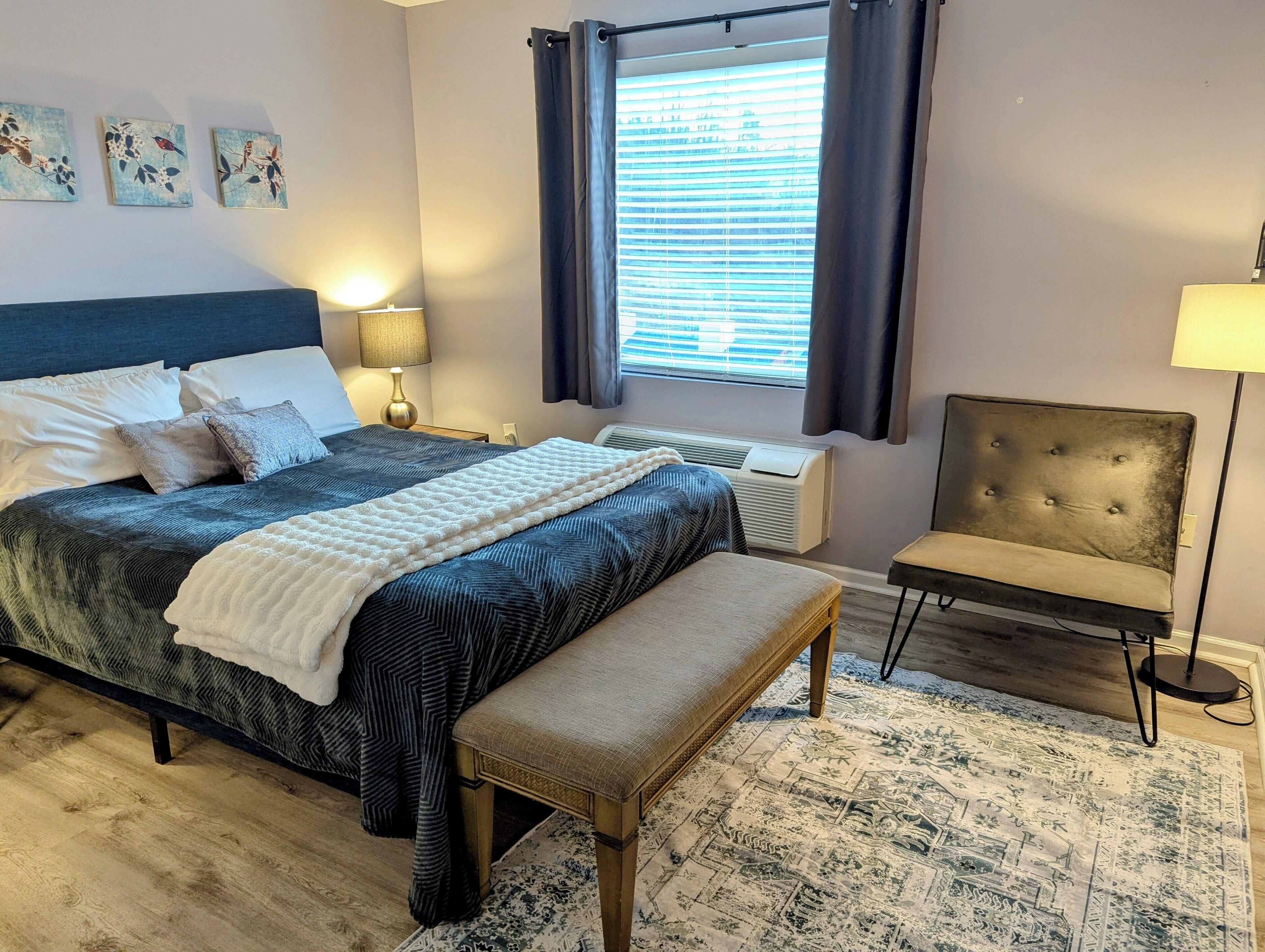 Ein Schlafzimmer mit Bett, Nachttischen, einer Bank, einem Sessel und Kunstwerken an der Wand.
