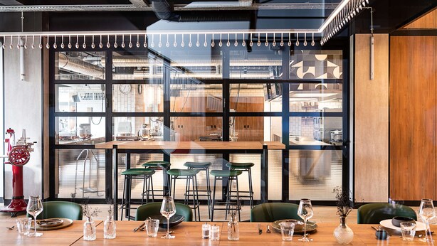 A modern dining area with a large window, wooden tables, and green chairs. - Campanile PRIME - Rungis Orly (Chevilly-Larue)