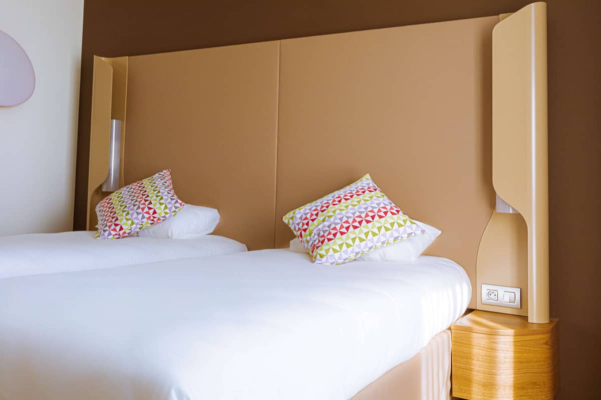 Habitación de hotel con dos camas, cada una con ropa blanca y almohadas de diseño geométrico y colores vivos.