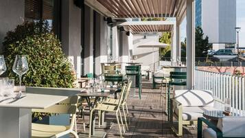 Une terrasse extérieure avec des tables et des chaises, un plafond en bois et une vue sur un bâtiment en arrière-plan.